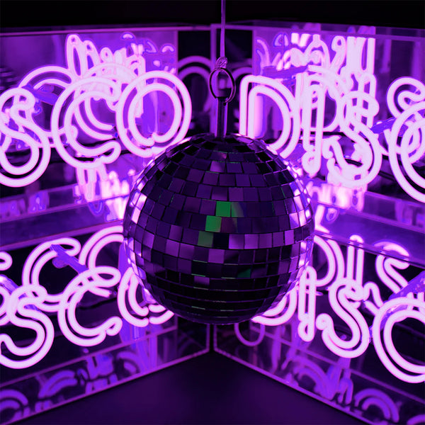 Neonschild "DISCO" im Hintergrund, Vordergrund eine Disco Kugel