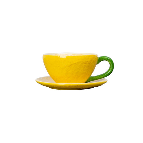 gelbe Teetasse mit untersetzer in der Optik einer Zitrone, grüner Henkel, Außenseite erinnert an eine Zitronenschale, Innenseite stellt das Fruchtfleisch der Zitrone dar