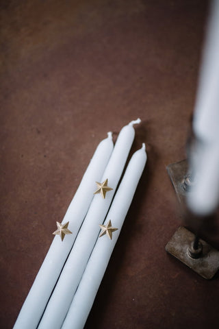 drei dünne weiße Kerzen mit jeweils einem goldenen Stern dekoriert
