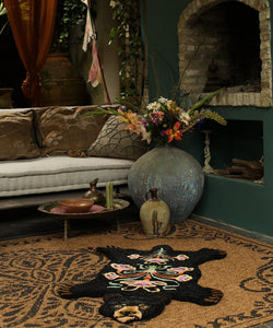 schwarzer Teppich in Form eines Baer mit bunten Blumen am Rücken, liegt in einem orientalisch anmutenden Raum am Boden