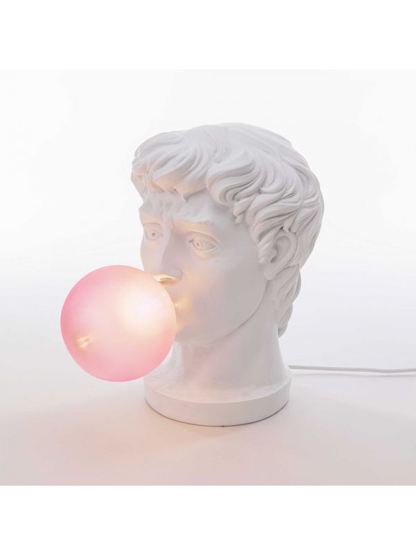 weißer Kopf einer antiken Statue des Gott Apollo, Glühbirne in Form einer pinken Kaugummiblase steckt im Mund